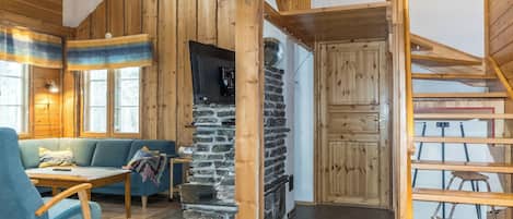 A cozy interior with a stone fireplace, wooden beams, a staircase, and a blue sofa.