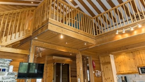 A spacious wooden interior with a balcony, stone wall, and a flat-screen TV.