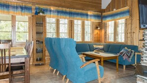 A wooden cabin interior with a dining area, blue upholstered seating, and a stone fireplace.