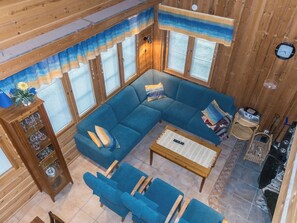 A log cabin interior with a blue sectional sofa, a wooden coffee table, and a glass cabinet with decorative items. - Lauri 4 iso by Interhome (Kittilä)