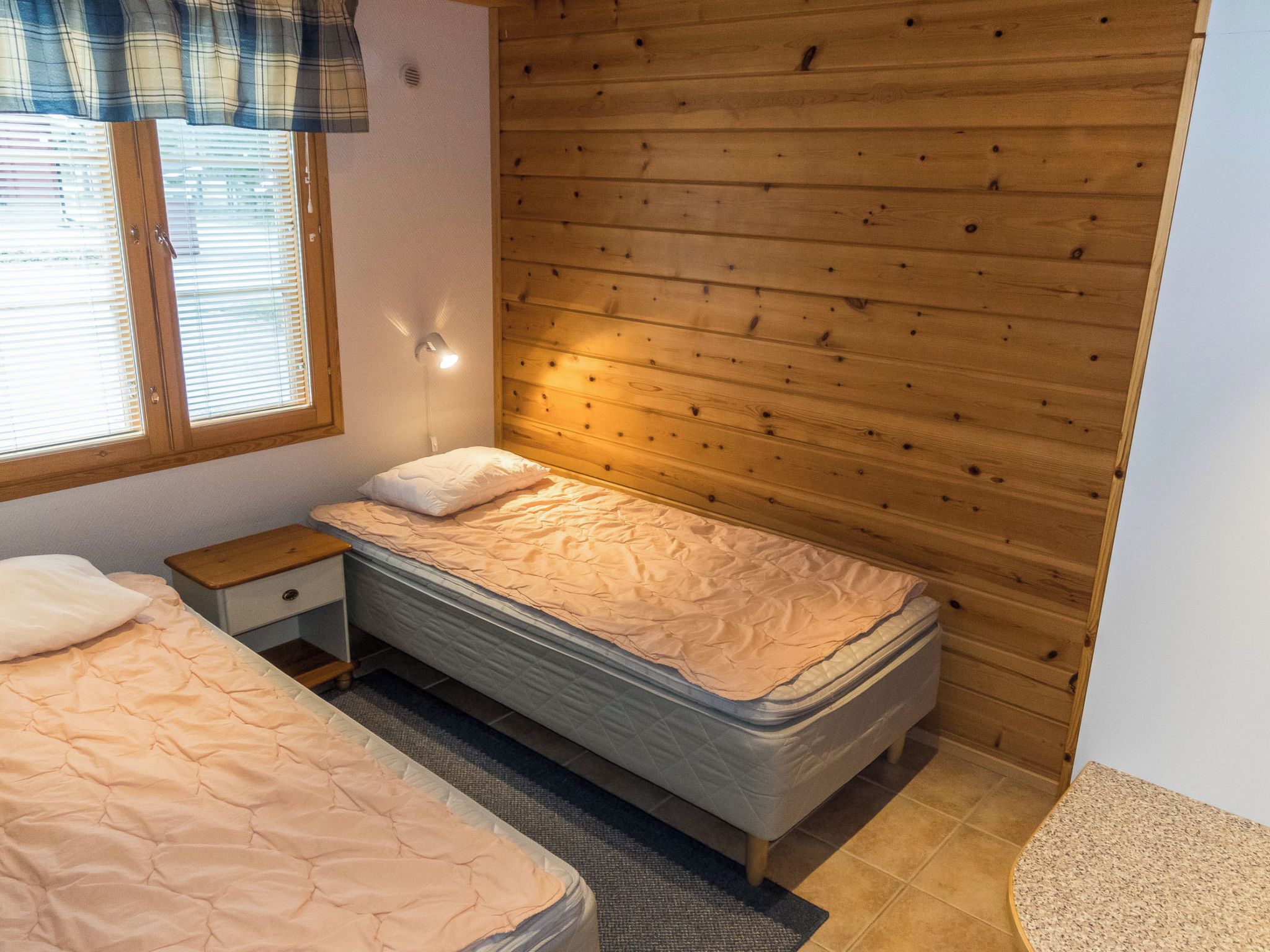 A bedroom with a bed, a nightstand, a window with blinds, and wooden paneling on the wall.