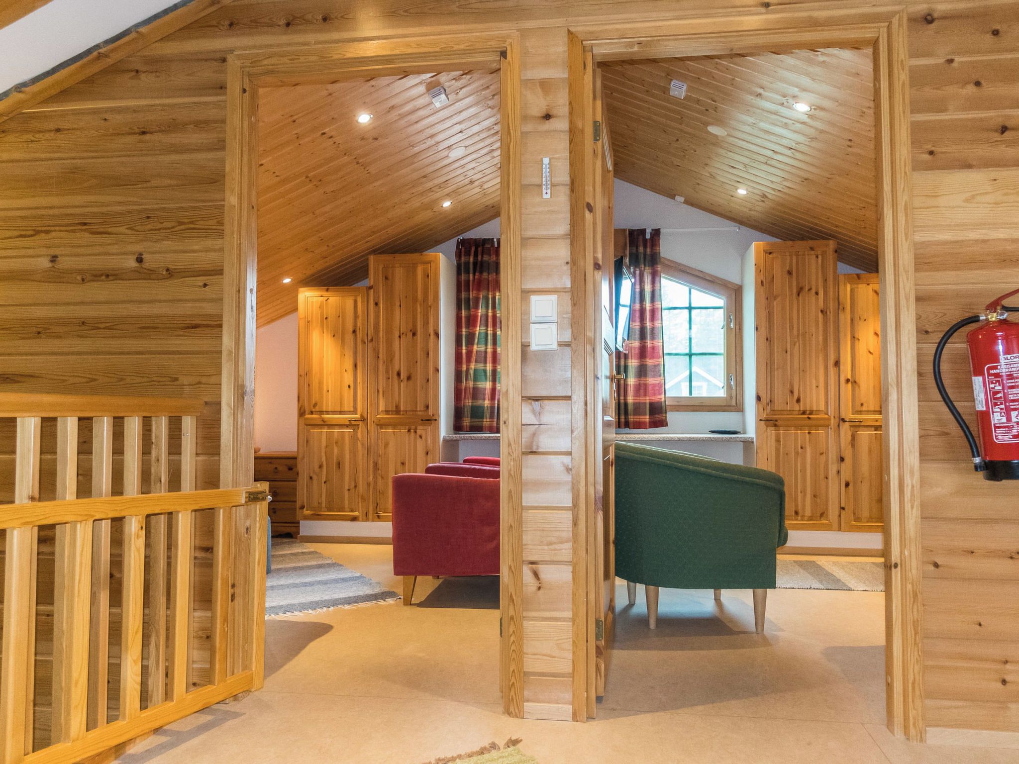 Un interior de madera con un dormitorio en entrepiso, una silla roja, una silla verde y un extintor.