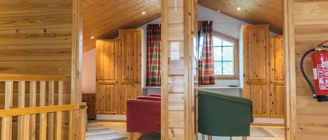Un interior de madera con un dormitorio en entrepiso, una silla roja, una silla verde y un extintor.