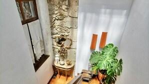 Una escalera con barandilla de madera, una pared de piedra con un espejo decorativo y una planta en maceta.