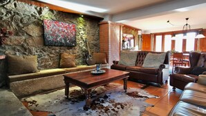 Una sala de estar acogedora con una pared de piedra, un sofá de cuero, una mesa de centro y un tapiz de piel de vaca.
