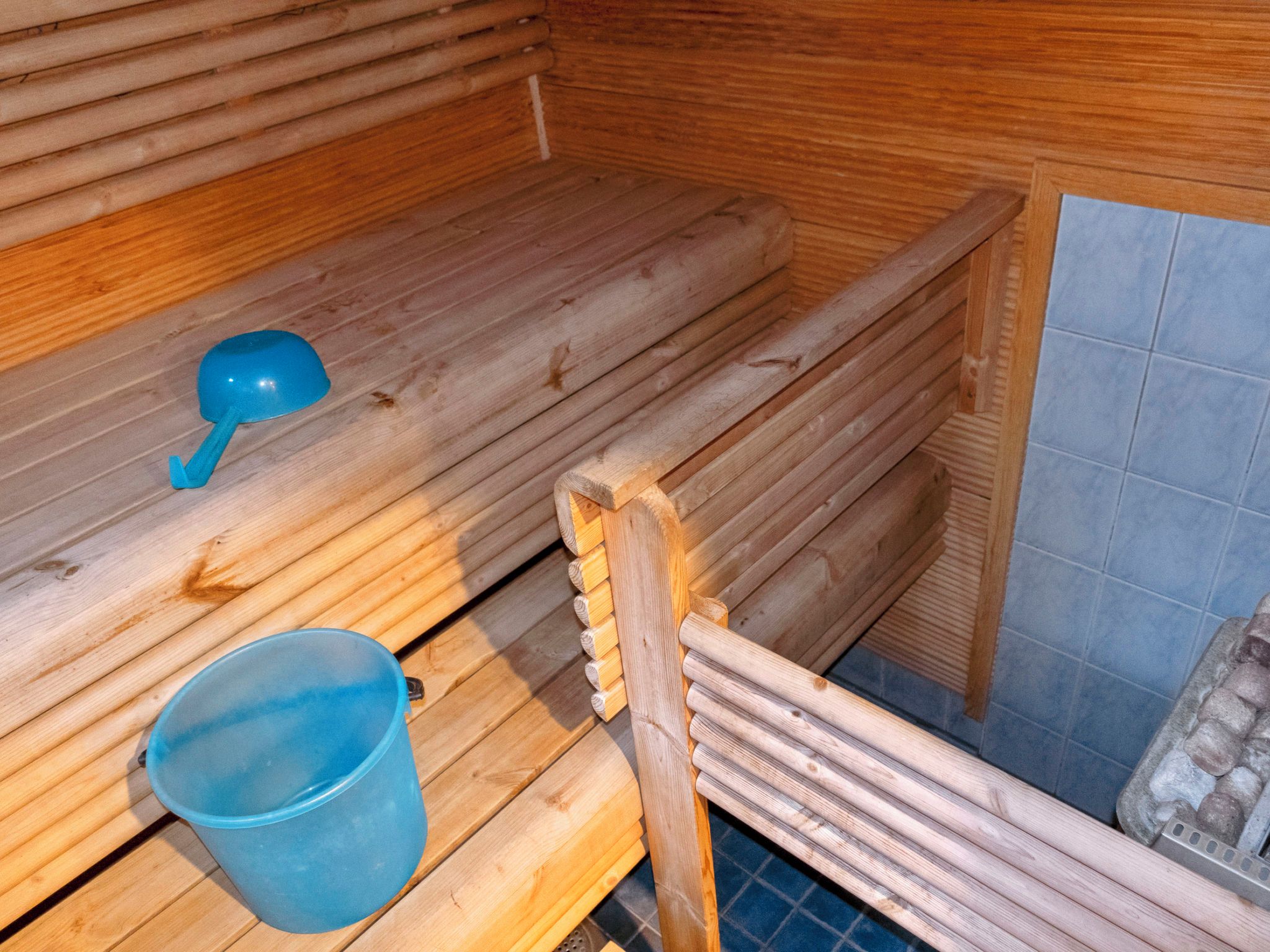 A sauna with wooden benches, a blue bucket, and a wooden structure.