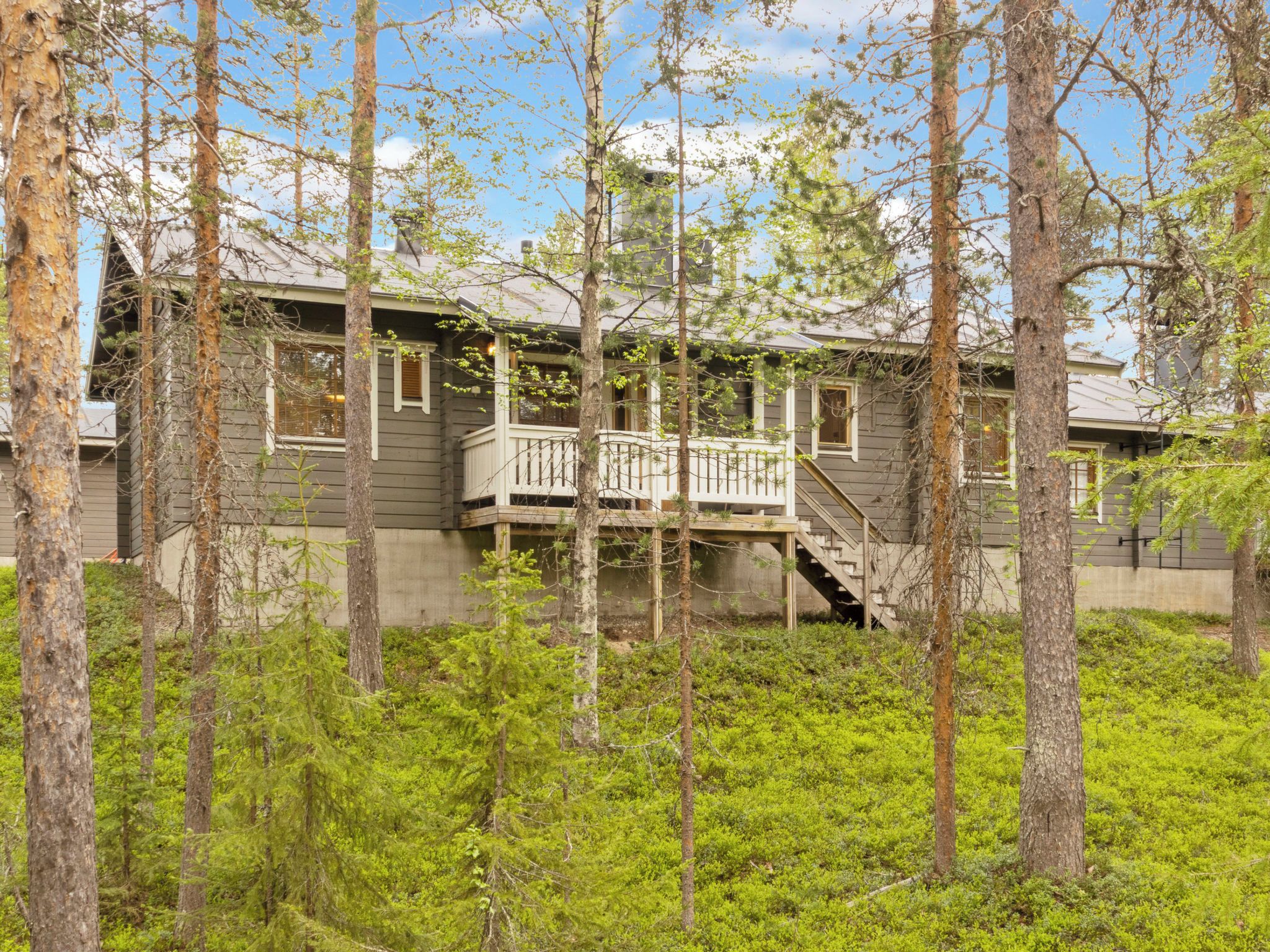 A two-story house with a balcony, surrounded by trees and greenery.