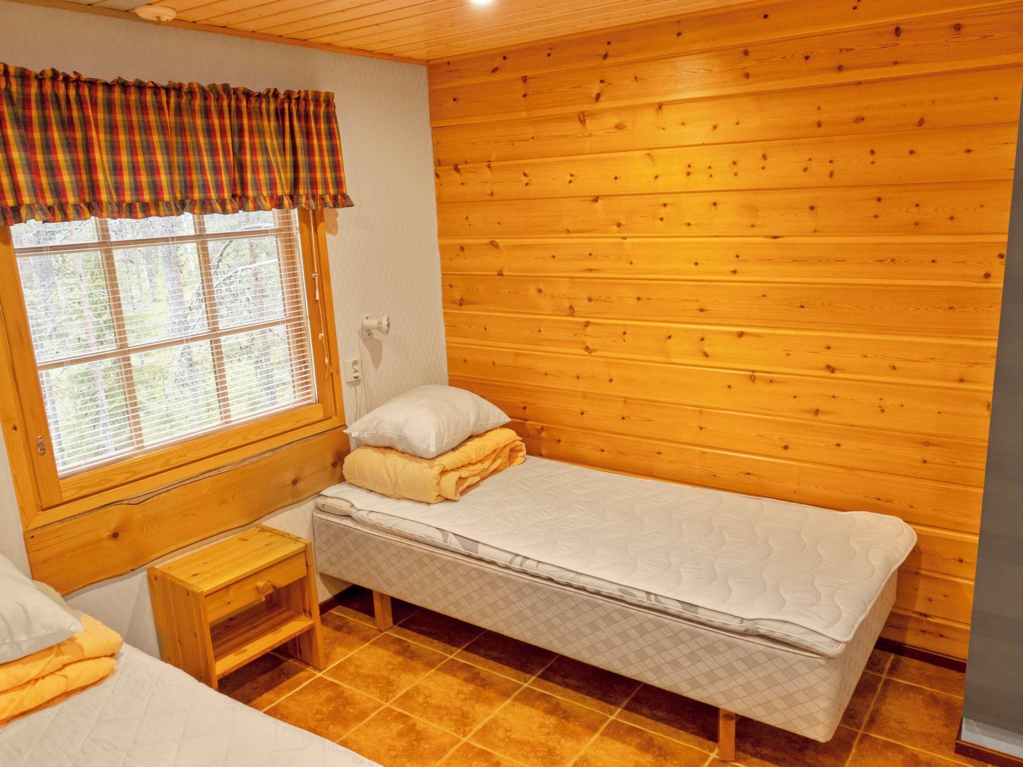 Une petite chambre agréable, dotée d’un lit simple, d’une table de chevet et d’une fenêtre avec des stores.