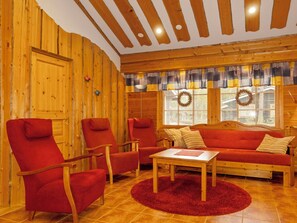 A cozy room with wooden walls, a red sofa, matching armchairs, and a wooden coffee table.