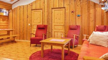 Une pièce chaleureuse avec des murs en bois, deux portes, un canapé rouge, une table en bois et un tapis rouge.