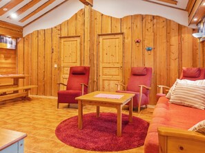 A cozy room with wooden walls, two doors, a red sofa, a wooden table, and a red rug. - Lauri 5 by Interhome (Kittilä)