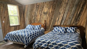 A room with two beds, wooden walls, and a window.