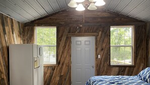 A cabin bedroom with a bed, a refrigerator, and two windows.