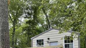 A small wooden cabin with a deck, a covered porch, and a staircase leading to the entrance.
