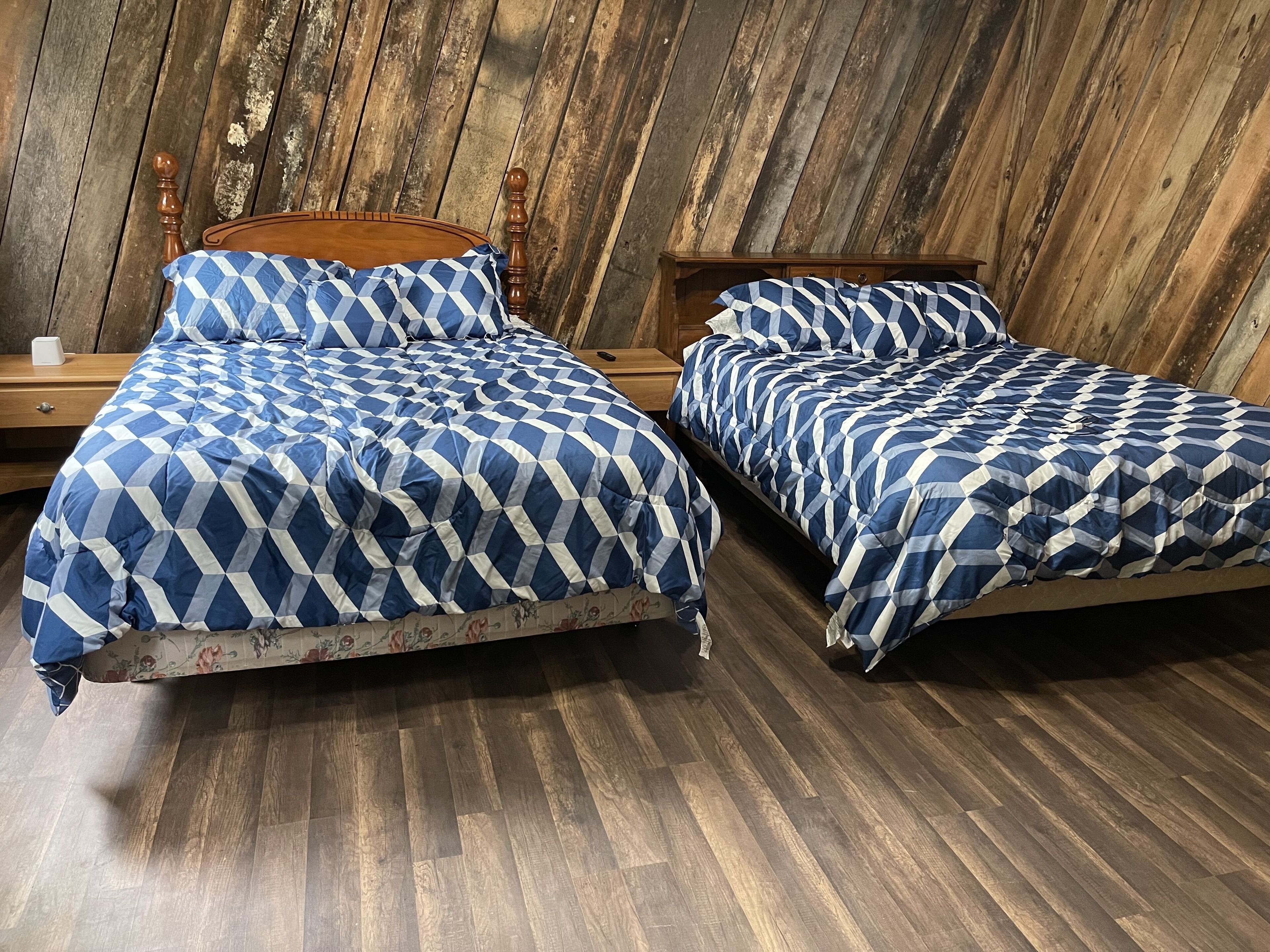 Two beds with blue and white checkered bedding, wooden headboards, and a wooden floor.