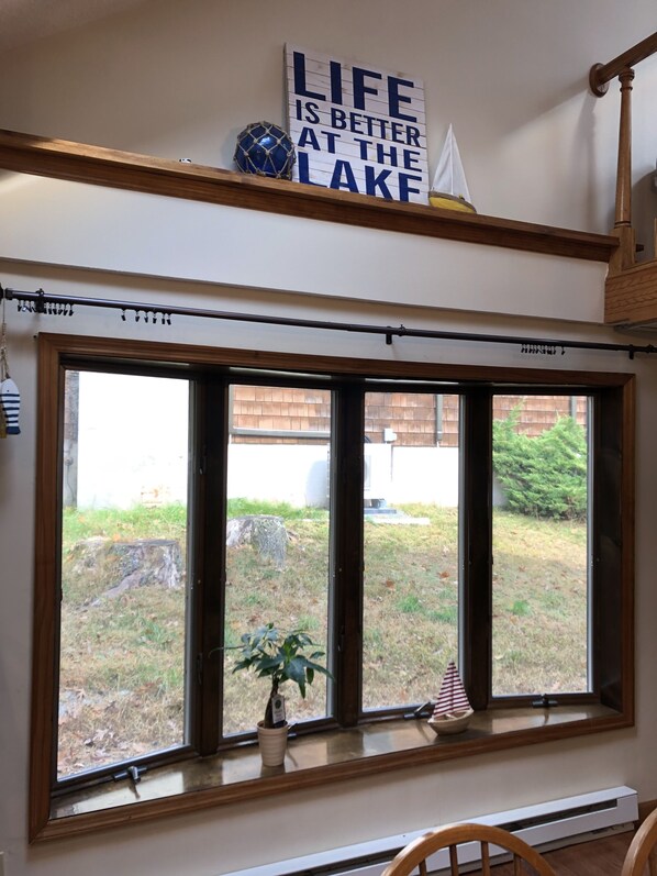 A room with a large window, a sign above reading "LIFE IS BETTER AT THE LAKE," a potted plant, and a small decorative item on the windowsill.