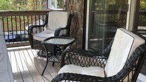 A covered outdoor seating area with wicker furniture and a stone wall backdrop. - Fire Pit, Babbling Brook, Poker & Foosball at this 3br+ home (Lakeville)