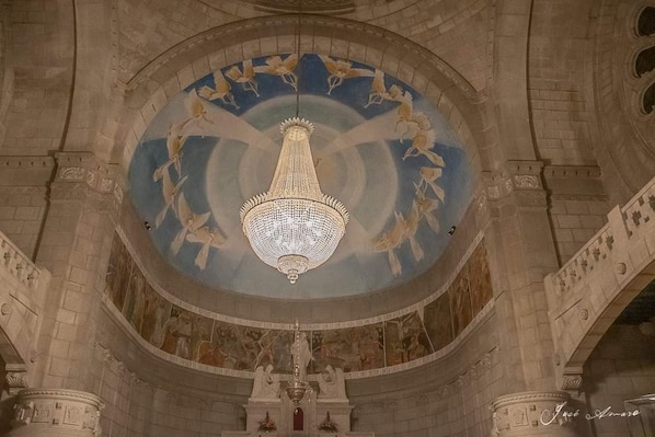 A grand hall with a large, ornate chandelier hanging from the ceiling, surrounded by detailed frescoes and classical architecture.