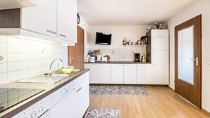 Une cuisine moderne avec des meubles blancs, un four encastré, un micro-ondes et un téléviseur placé au-dessus du plan de travail.