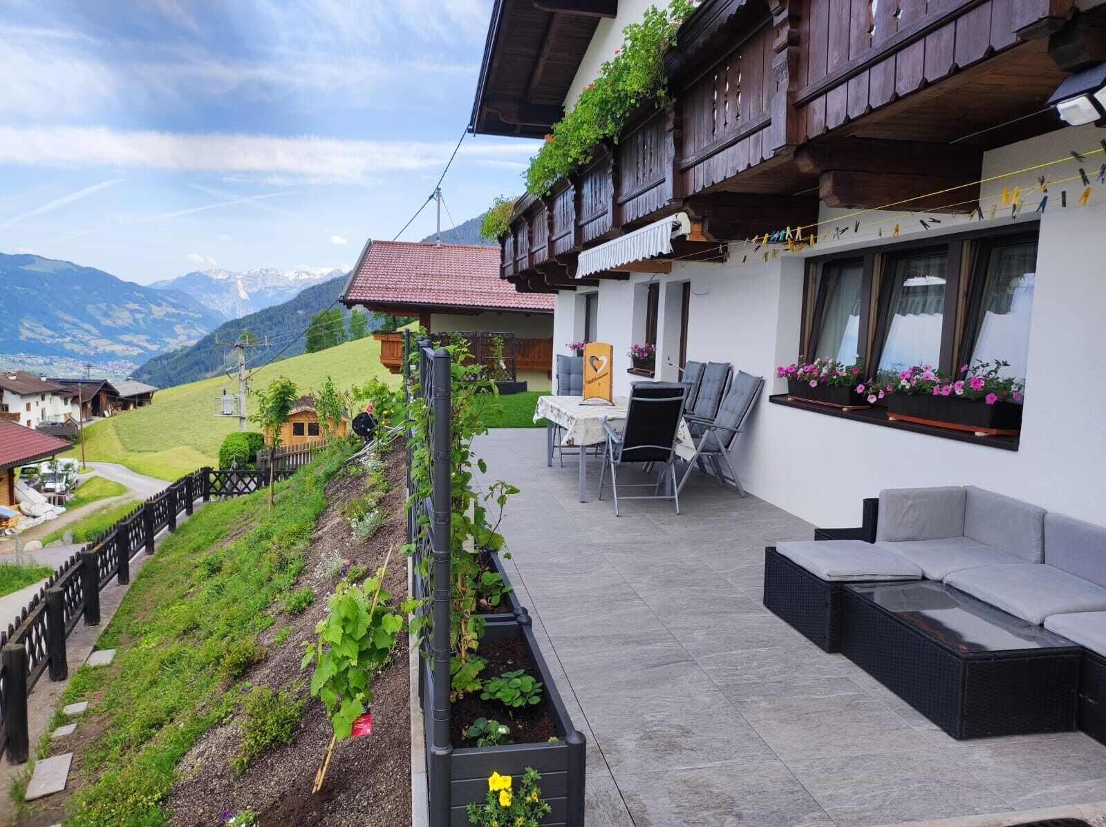A balcony with outdoor furniture, a garden, and a mountain view.