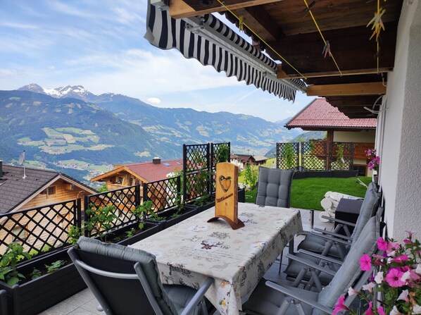 Eine Terrasse mit Tisch und Stühlen, ein hölzerner Pfosten mit einem Herz und Blick auf die Berge.