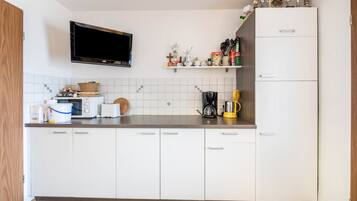 Een keuken met witte kasten, een magnetron, een koffiezetapparaat en een televisie boven de toonbank.