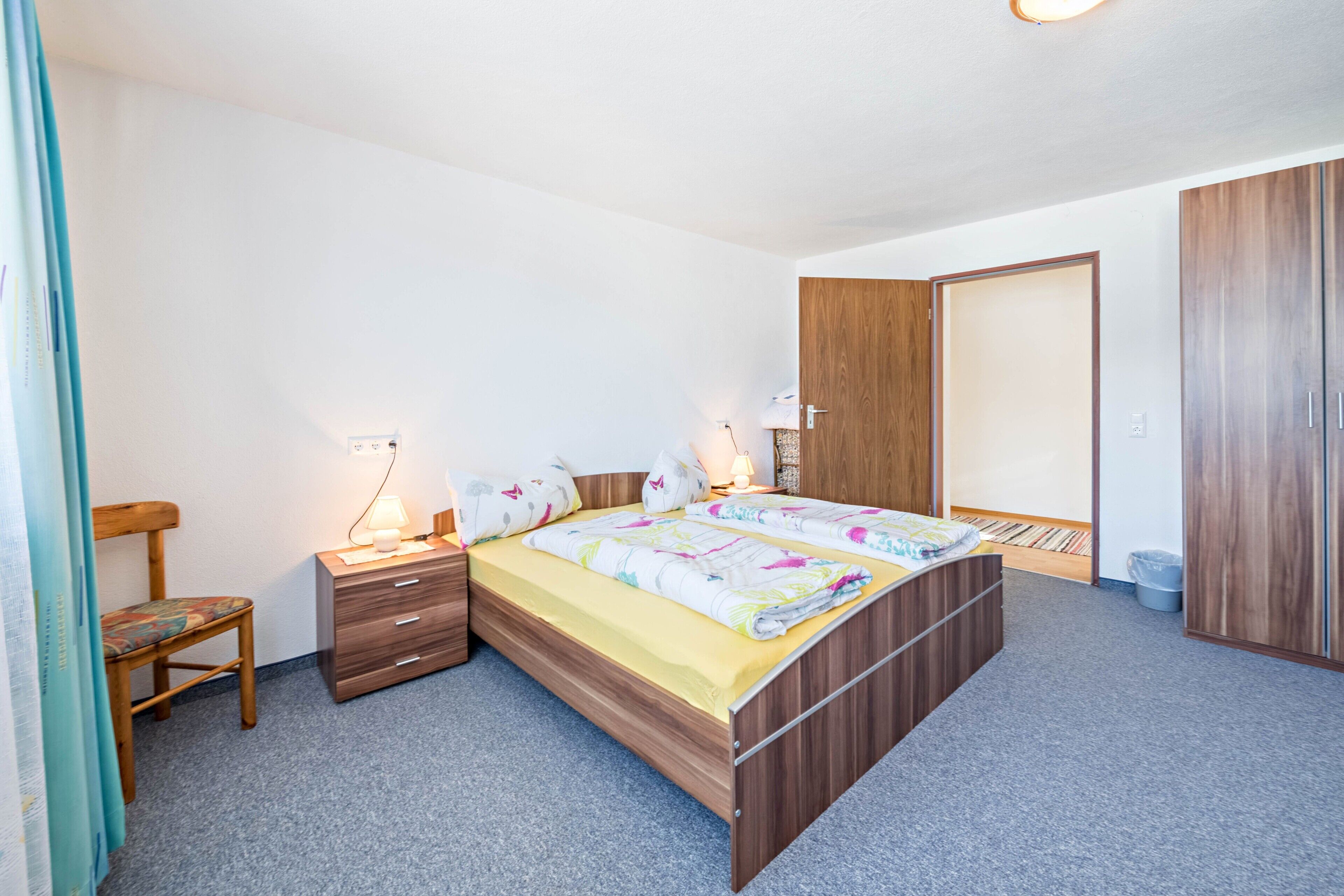 Une chambre à coucher avec un lit, des tables de chevet, une chaise, une armoire et une porte.