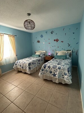 Une chambre avec deux lits, un luminaire suspendu et un mur décoré d’autocollants représentant des motifs marins.