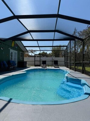 Une piscine dotée d’une zone abritée, de chaises longues et d’un bâtiment en arrière-plan.
