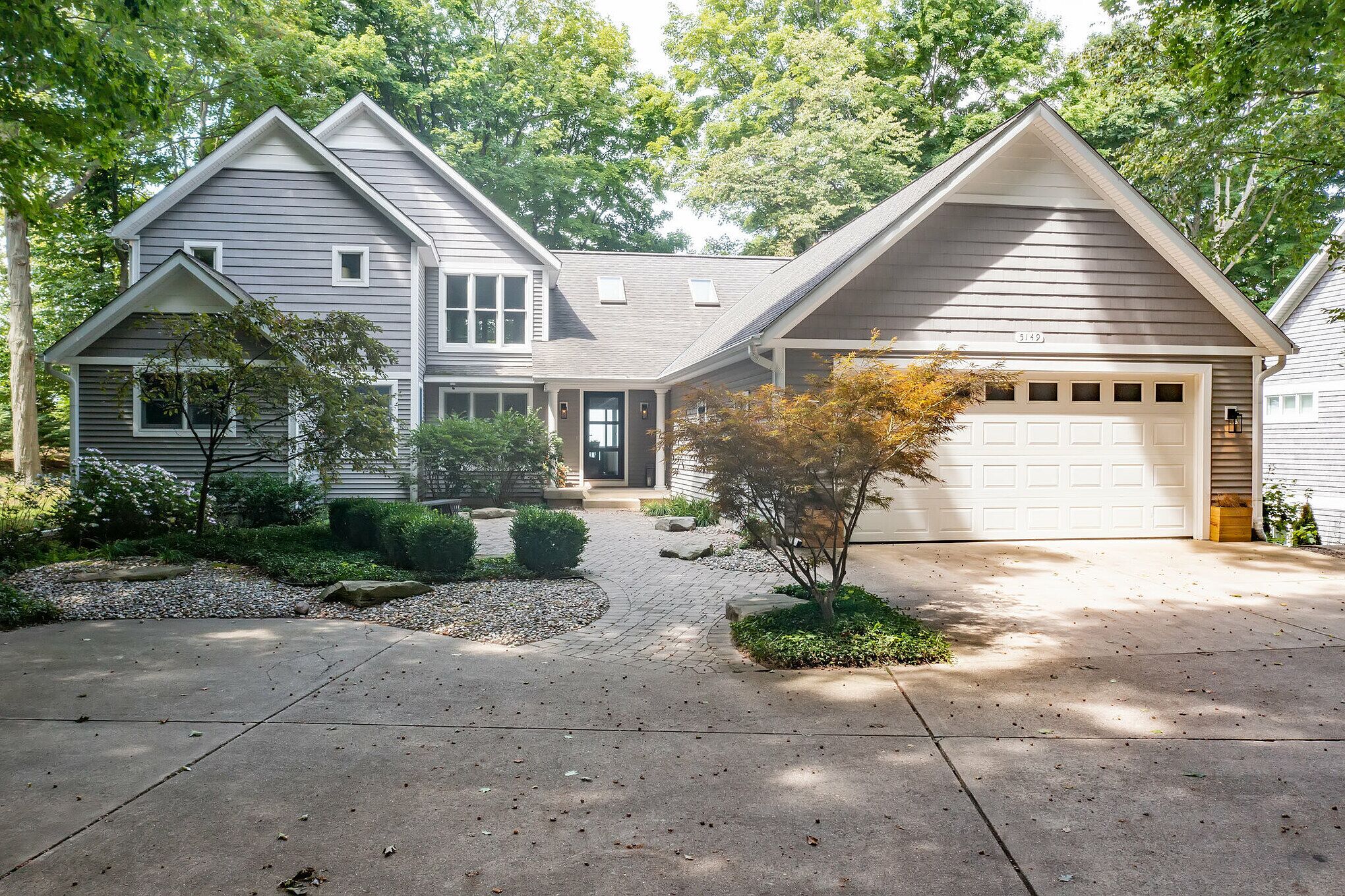 A two-story house with a garage, surrounded by trees and a landscaped driveway.