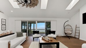 Amplia sala de estar con un sofá blanco, una mesa de centro y un sillón colgante. Hay un ventanal con vista al mar.