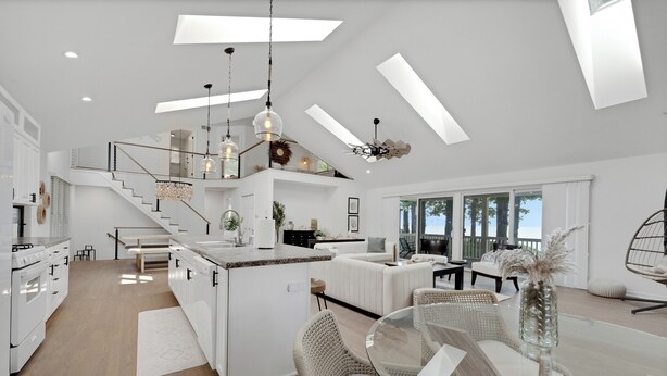Cocina amplia y moderna con una isla central, un comedor con mobiliario de mimbre y vistas al exterior a través de grandes ventanales.