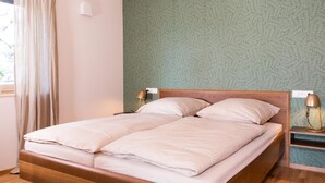 A double bed with a wooden frame, two bedside tables with lamps, a window with curtains, and a patterned wall. - Apartment "Anneliese" with Terrace, Garden & Wi-Fi (Neukirch)