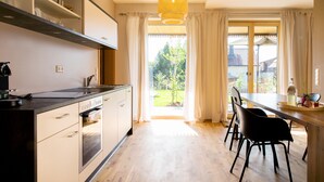 A modern kitchen with built-in appliances, a dining area with chairs, and a view of the outdoors. - Apartment "Anneliese" with Terrace, Garden & Wi-Fi (Neukirch)