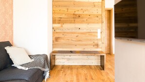 A room with a wooden wall panel, a sofa with a cushion, and a flat-screen TV. - Apartment "Anneliese" with Terrace, Garden & Wi-Fi (Neukirch)