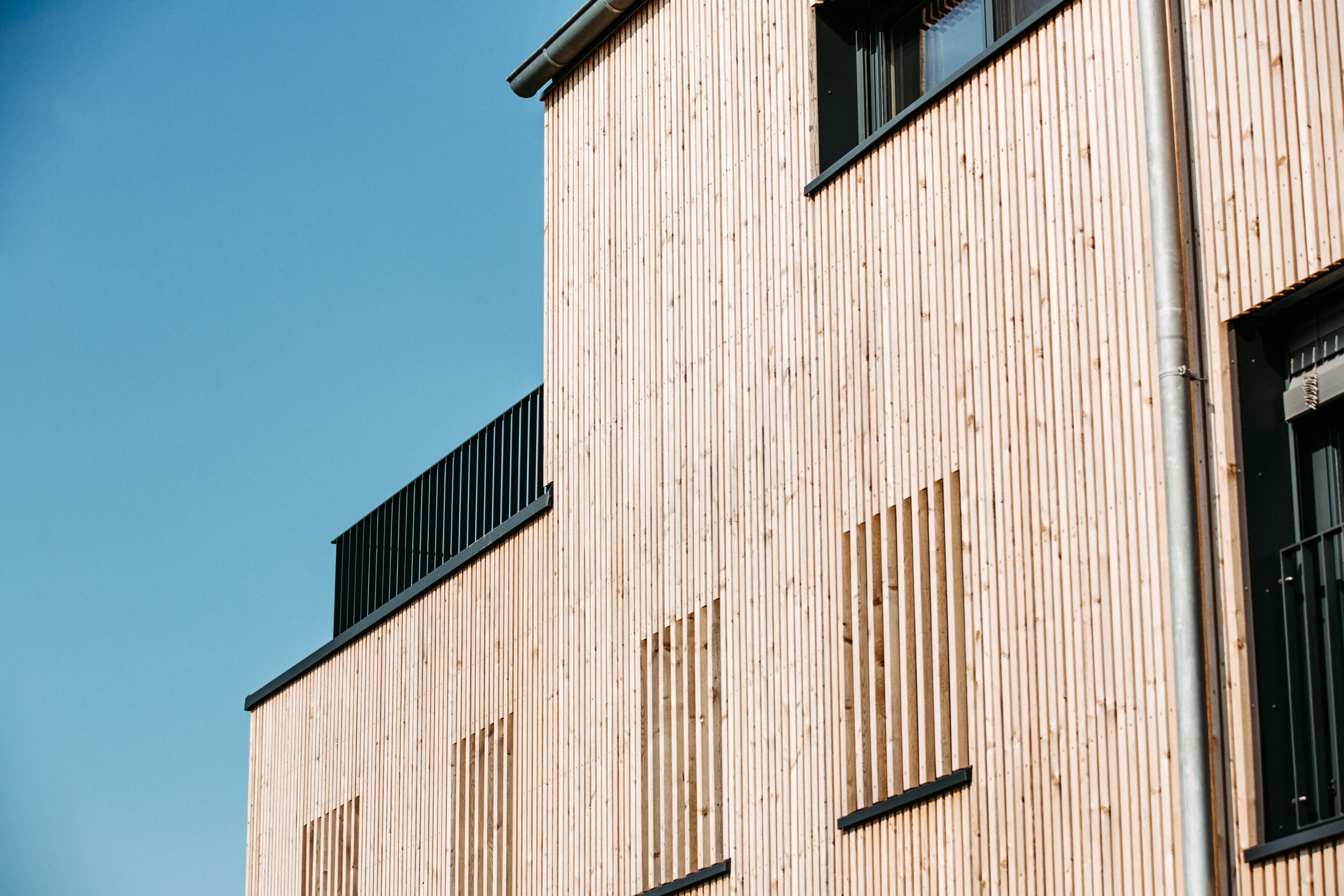 Un bâtiment doté de panneaux de bois verticaux, de cadres de fenêtres noirs et surplombé d’un ciel bleu clair.