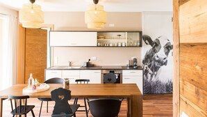 A modern kitchen with white cabinets, a wooden dining table, black chairs, and a large wall-mounted picture of a cow. - Holiday Apartment "Liselotte" with Terrace, Garden & Wi-Fi (Neukirch)