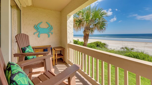 Un balcone con mobili in legno, un'opera decorativa raffigurante un granchio e vista sulla spiaggia.