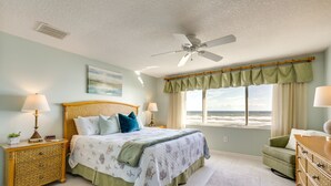 Una camera da letto con un letto, due comodini con lampade, una cassettiera, una sedia e vista sull'oceano attraverso una finestra.