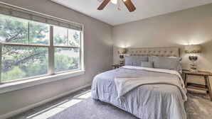 A bedroom with a large window, a bed, a ceiling fan, and a nightstand with a lamp. - Charming Springdale Townhome ~ 5 Mi to Dtwn! (Springdale)