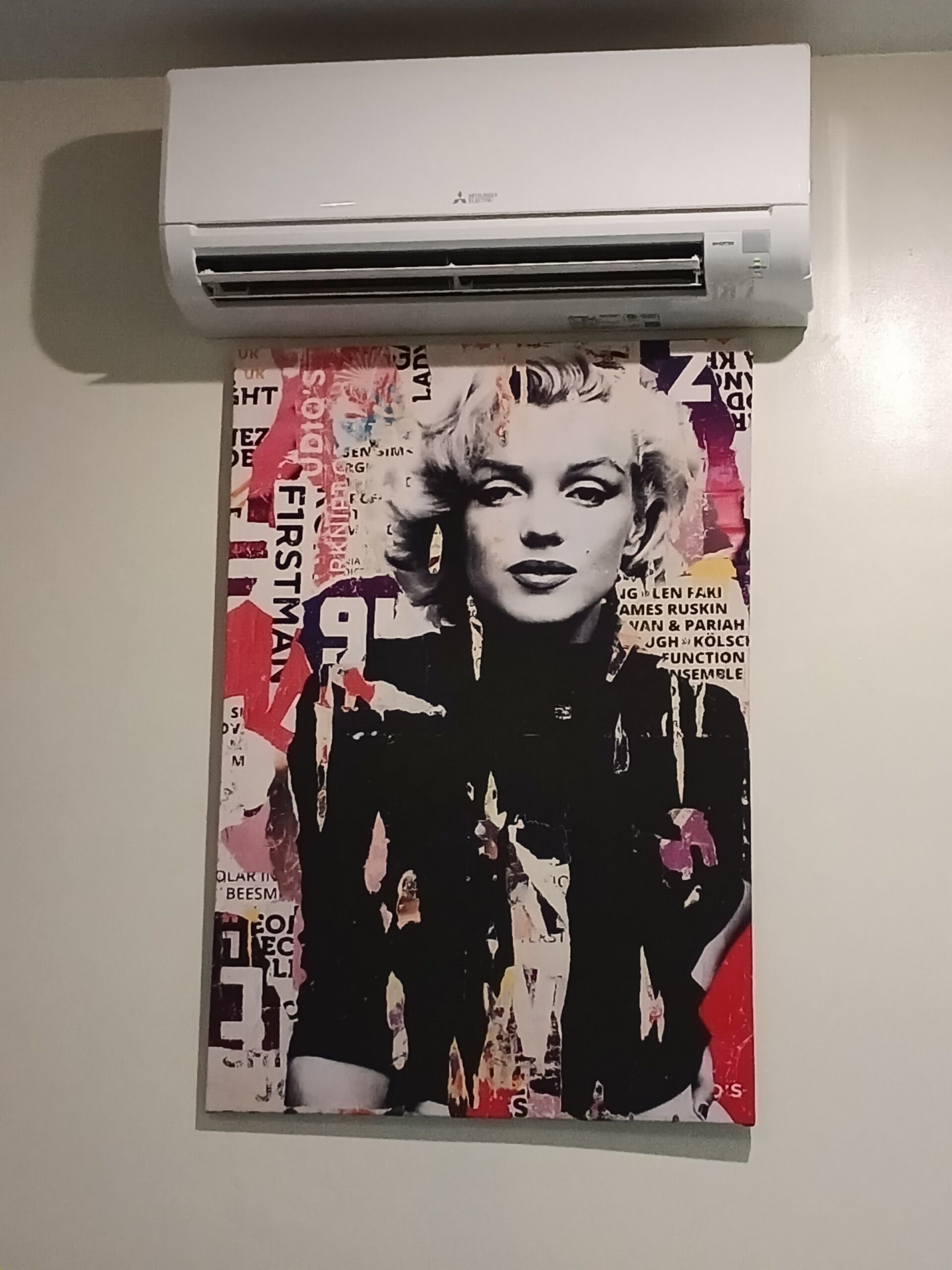 A wall-mounted air conditioning unit above a poster with text and a partially visible figure.