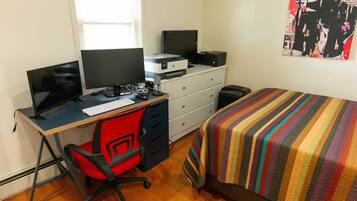 Une chambre à coucher avec un lit, un bureau avec un ordinateur, une chaise, une commode et une affiche accrochée au mur.