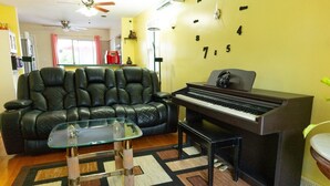 Un salon avec un canapé en cuir noir, une table basse en verre, un piano et une horloge murale.