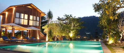 Una villa de madera con piscina, sillas de descanso y sombrillas.
