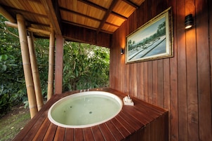 Un'area spa in legno con vasca idromassaggio, elementi in bambù e un quadro appeso alla parete.