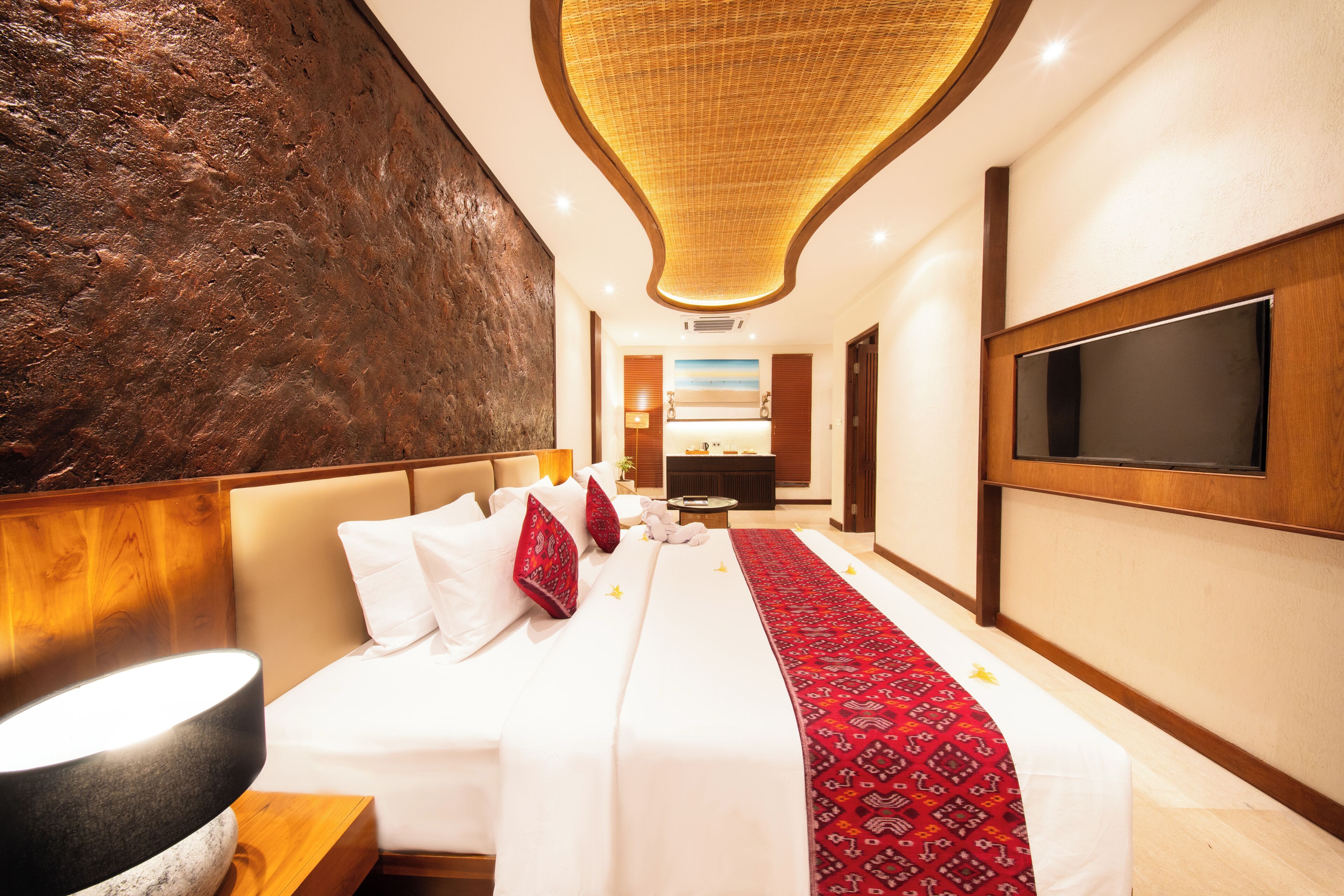A hotel room with a large bed, a flat-screen TV, a modern ceiling design, and a large wall with a textured surface.