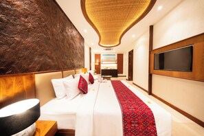 A hotel room with a large bed, a flat-screen TV, a modern ceiling design, and a large wall with a textured surface.
