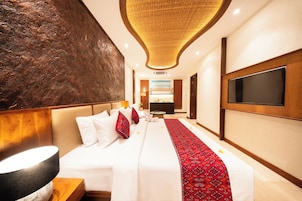 Una camera d'hotel con un letto grande, una TV a schermo piatto, un design moderno del soffitto e una parete ampia con superficie strutturata.
