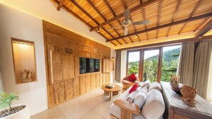 Amplia sala de estar con televisor grande, panel de madera, asientos cómodos y vista a zonas verdes.