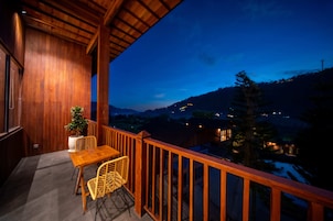 Un balcone in legno con tavolo e sedie, affacciato su un paesaggio montuoso al crepuscolo.